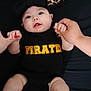Madison is registered to the contest to win money with this photo: baby, infant, black_clothing, headband, bow, leopard_print, hands, holding_hands, lying_down, socks, floor, footwear, nike_slides, person, child, indoor, cute, expression, black_background, text_on_clothing