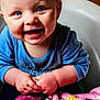 baby, child, blue_eyes, smile, happy, blanket, clothing, sitting, hands, face, cute, infant, portrait, indoors, warm_colors, furniture, person, cozy, expression, closeup
