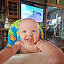 baby, child, smiling, high_chair, indoor, home, television, cartoon, furniture, person, happy, blue_eyes, bald, reaching, colorful, kitchen, living_room, smile, infant, cute