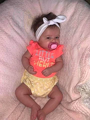 Maisie is registered to the contest to win money with this photo: abdomen, baby, baby_products, baby_toddler_clothing, cheek, child, comfort, costume, day_dress, eye, fun, headwear, linens, pattern, person, pink, sitting, sleeve, sun_hat, thigh