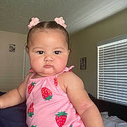 Aaliyah joined the competition — help win amazing prizes! baby, child, pink_clothing, strawberry_pattern, hair_clips, indoor, bedroom, window_blinds, face, portrait, cute, chubby_cheeks, curly_hair, infant, person, sitting, soft_lighting, expression, young_child, casual_wear