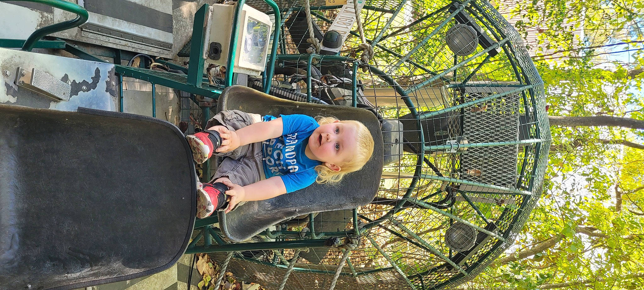 Elijah is registered to the contest to win money with this photo: auto_part, automotive_exterior, automotive_tire, automotive_wheel_system, child, city, fun, grass, leisure, mesh, metal, motor_vehicle, outdoor_play_equipment, plant, recreation, sitting, spoke, t_shirt, toddler, tree