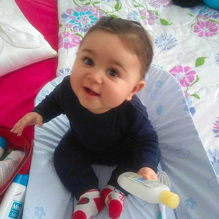 Yazid participe au concours pour gagner de l'argent avec cette photo : baby, baby_care, bedspread, bottle, changing_mat, child, clothing, cute, face, furniture, happy, healthcare, indoor, infant, person, pillow, sitting, smiling, socks, toy