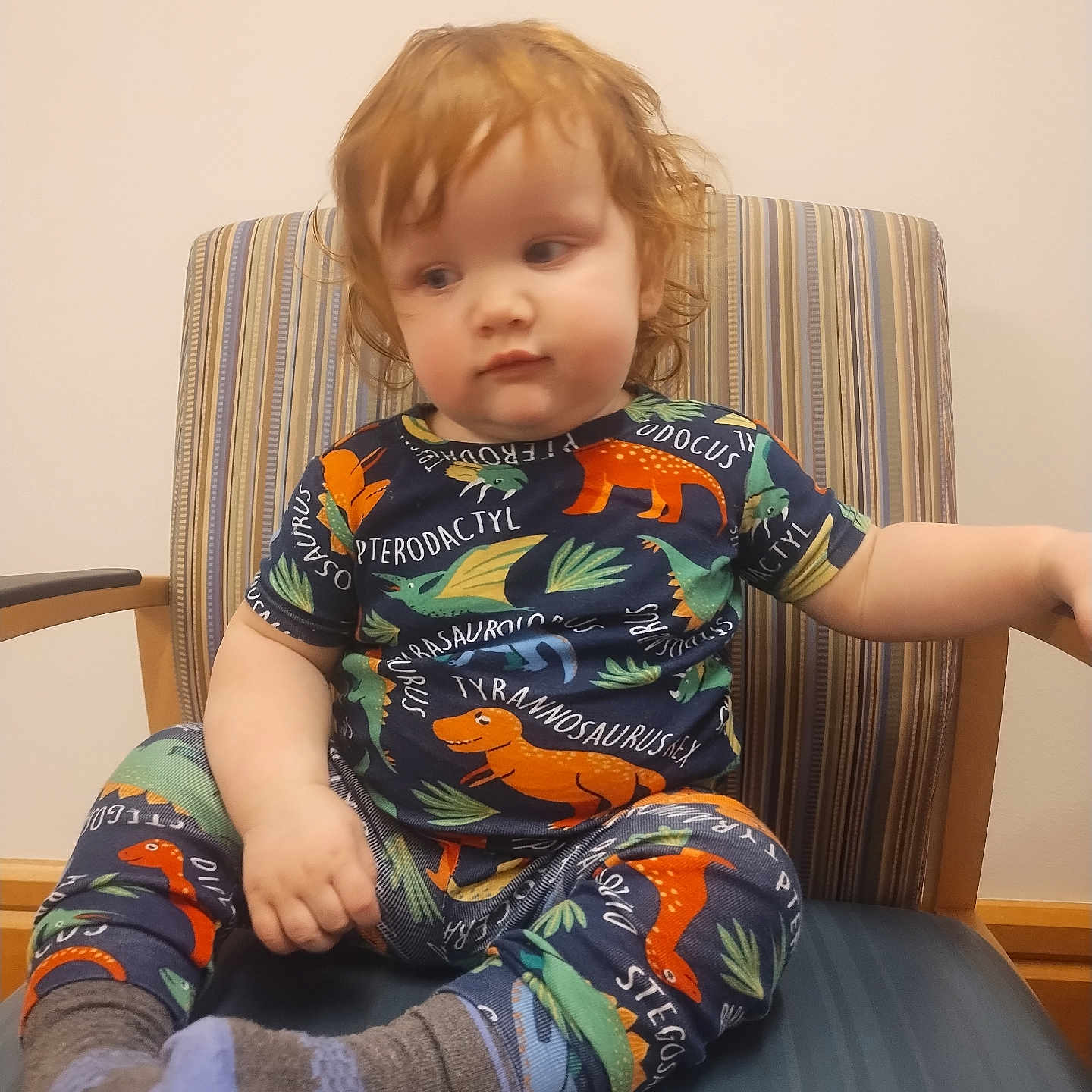 Willow joined the competition — help win amazing prizes! toddler, child, curly_hair, red_hair, dinosaur_clothing, striped_chair, socks, indoor, seated, thoughtful, cute, young_child, casual, comfortable, portrait, person, furniture, home, colorful, playful