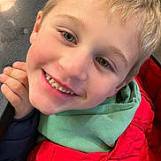 Enzo a rejoint le concours — aidez-le/la à gagner de superbes lots ! child, smiling, face, blonde_hair, red_jacket, green_hoodie, happy, indoor, portrait, closeup, hand, casual_clothing, person, young, cute, apparel, warm_clothes, kid, joyful, expression