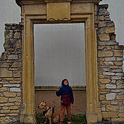 Tania a rejoint le concours — aidez-le/la à gagner de superbes lots ! child, dog, stone_archway, outdoor, fall_leaves, jacket, hoodie, sneakers, historic, wall, sidewalk, leash, pet, brown_dog, standing, sitting, old_stone, casual_clothing, urban, friendship