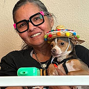 Agador Spartacus is registered to the contest to win money with this photo: accessories, animal, black_shirt, casual, colorful, dog, face, glasses, happy, hat, holding, indoor, jewelry, person, pet, portrait, smiling, sombrero, watch, woman
