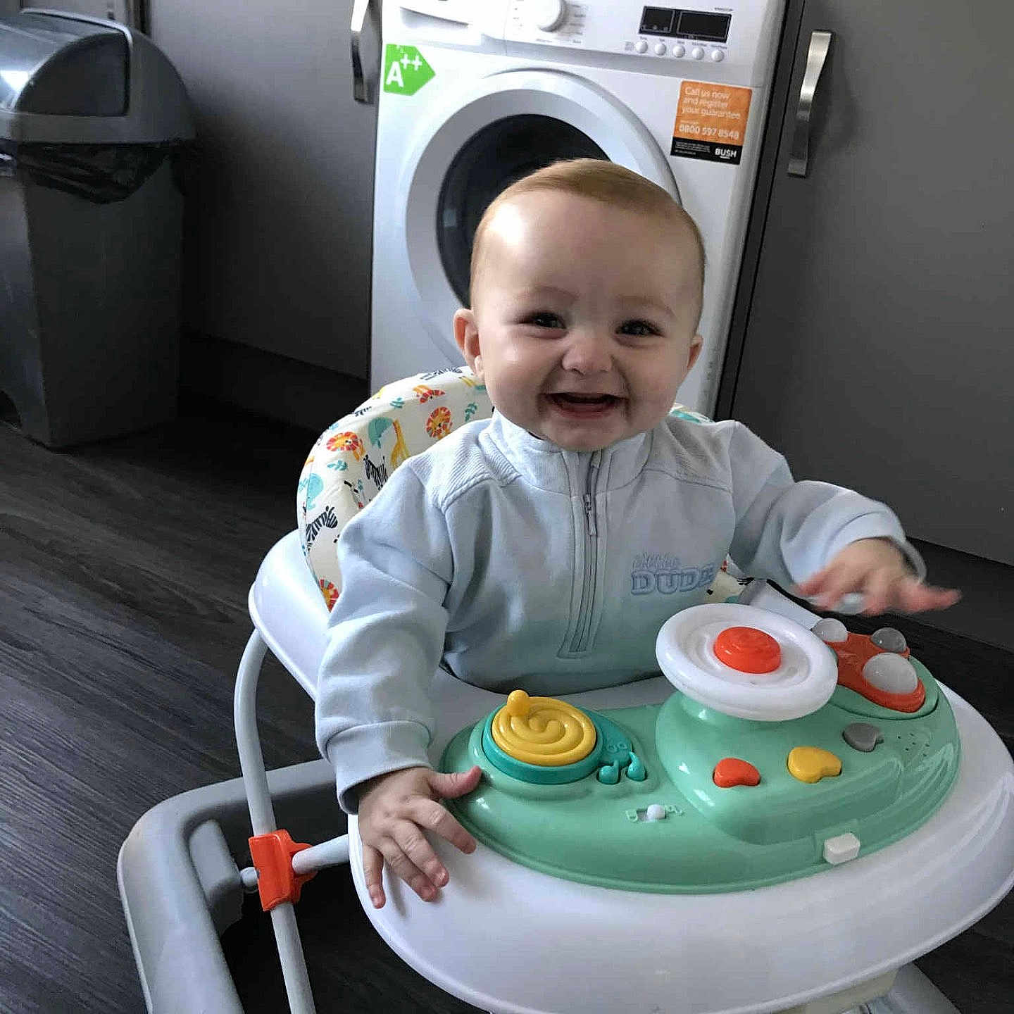 Cobi-Jai is registered to the contest to win money with this photo: appliance, baby, cabinet, child, clothing, face, floor, furniture, hand, happy, head, indoor, kitchen, person, playing, smiling, toy, trash_bin, walker, washing_machine