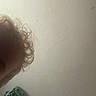 child, curly_hair, close_up, partial_face, indoor, wall, beige, blurry, hair, head, person, young, kid, background, texture, corner, casual, unfocused, portrait, indoor_lighting