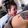 baby, infant, child, smiling, laughing, portrait, close_up, indoor, candid, adult, parent, tattoo, arm, onesie, blanket, cuddling, happy, face, home, soft_lighting