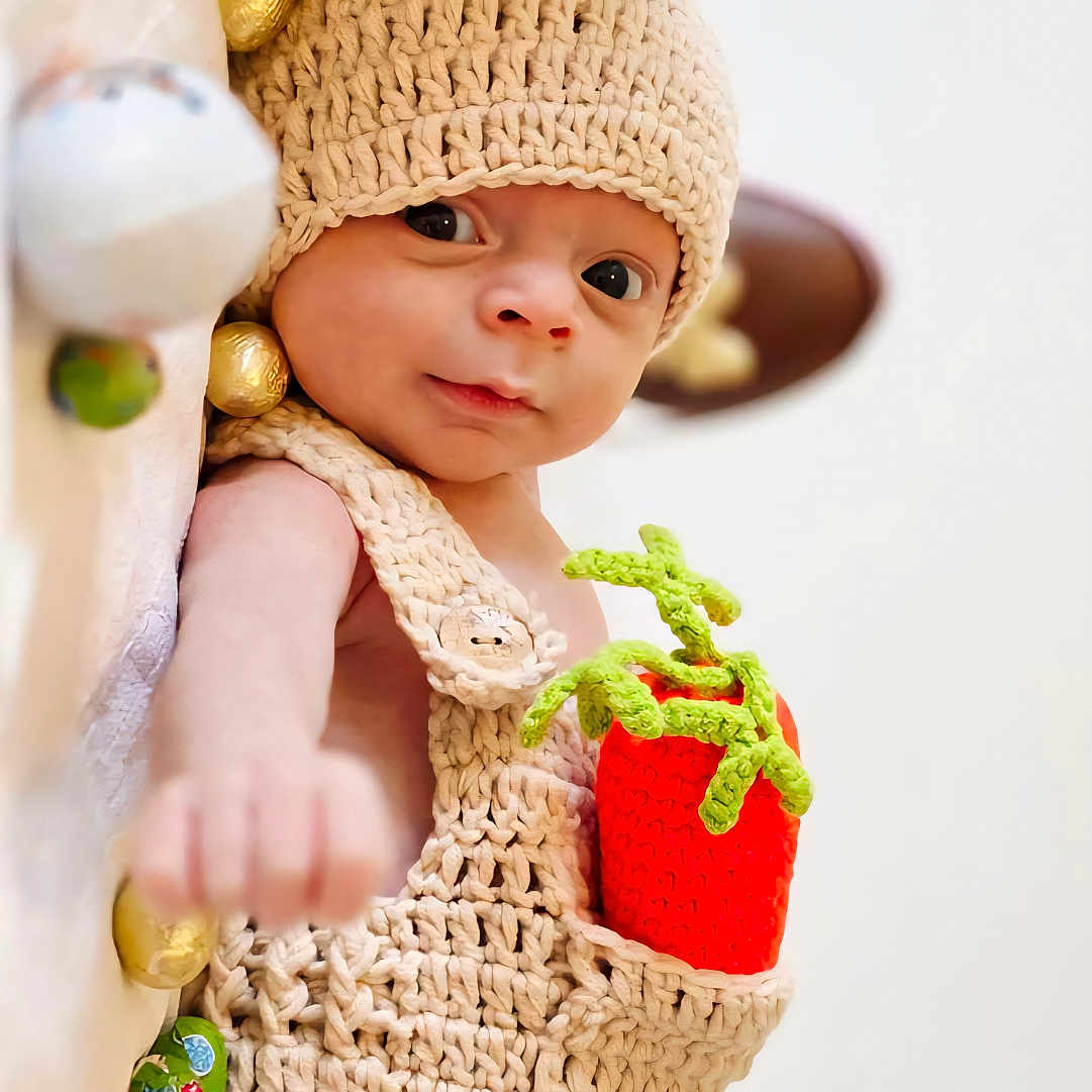 Mahé a rejoint le concours — aidez-le/la à gagner de superbes lots ! baby, infant, knitted_clothing, hat, carrot, toy, chocolate, wrapped_candy, cute, portrait, lying_down, soft_surface, hand, expression, colorful, closeup, child, indoors, warm, cozy