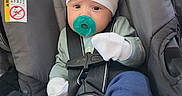 Ezra is registered to the contest to win money with this photo:  안전, adorable, awake, baby, beanie, blue_clothing, car_seat, child, close_up, harness, indoors, infant, mittens, pacifier, portrait, seatbelt, seated, shoes, socks, vehicle