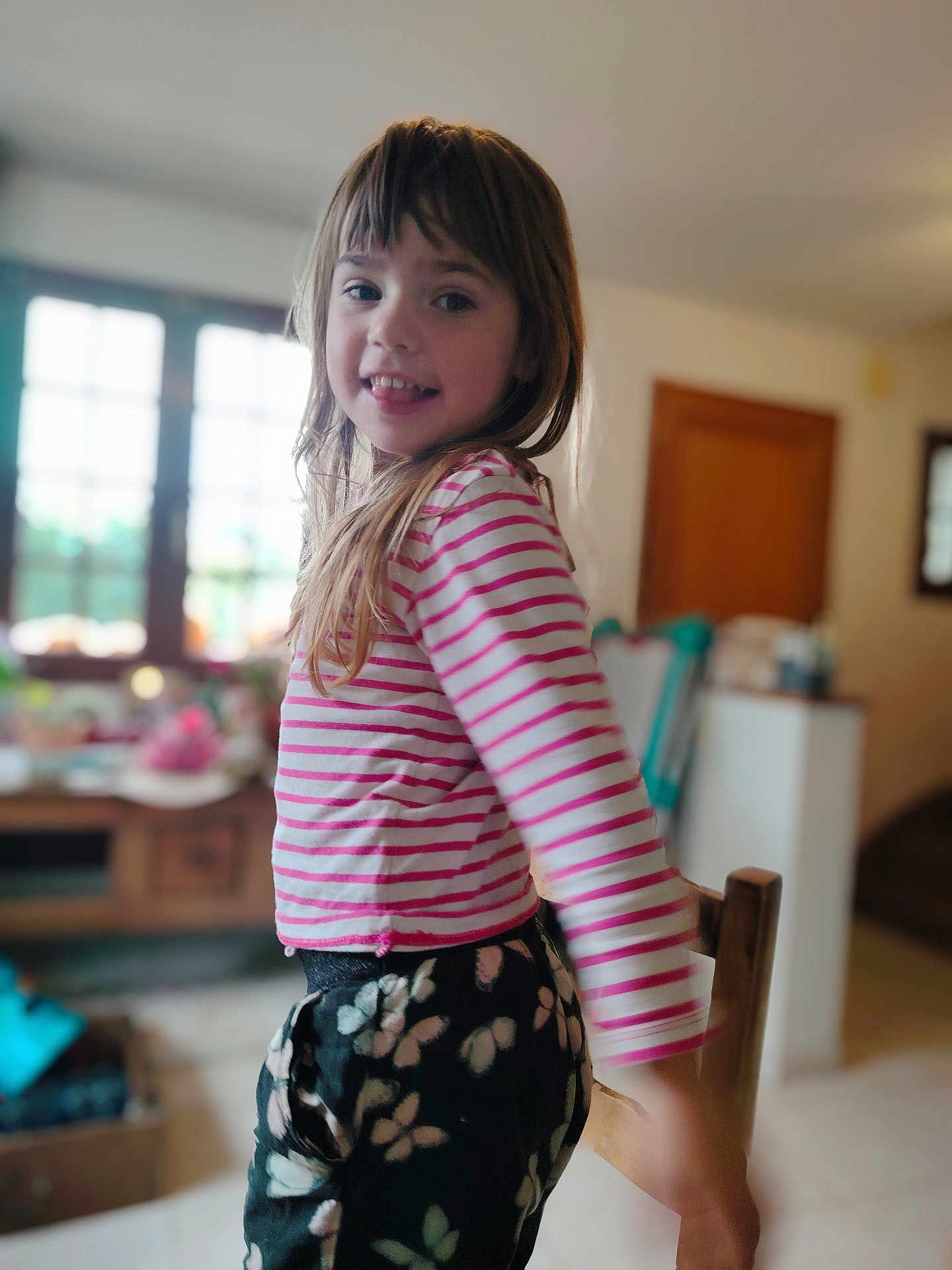 Savannah participe au concours pour gagner de l'argent avec cette photo : child, girl, smiling, indoor, striped_shirt, pink, white, floral_pants, long_hair, happy, portrait, person, home, window, furniture, wooden_chair, casual_clothing, daylight, playful, cute