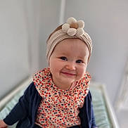 Ruby a rejoint le concours — aidez-le/la à gagner de superbes lots ! apparel, baby, child, closeup, colorful, cute, face, flower, happy, headband, headwear, indoor, infant, patterned_clothing, person, portrait, sitting, smiling, soft_background, young_child