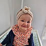 apparel, baby, child, closeup, colorful, cute, face, flower, happy, headband, headwear, indoor, infant, patterned_clothing, person, portrait, sitting, smiling, soft_background, young_child