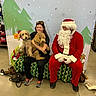 Chester is registered to the contest to win money with this photo: woman, dog, person, santa_claus, christmas, holiday, bench, indoor, decor, festive, costume, pet, canine, smile, seated, background, tree, snowflake, leash, floor