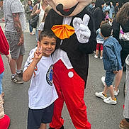 Borhan participe au concours pour gagner de l'argent avec cette photo : child, costume, character, peace_sign, outdoor, crowd, festival, smiling, boy, person, street, casual_clothing, red_pants, white_shirt, black_jacket, footwear, tattoo, background_people, daytime, event