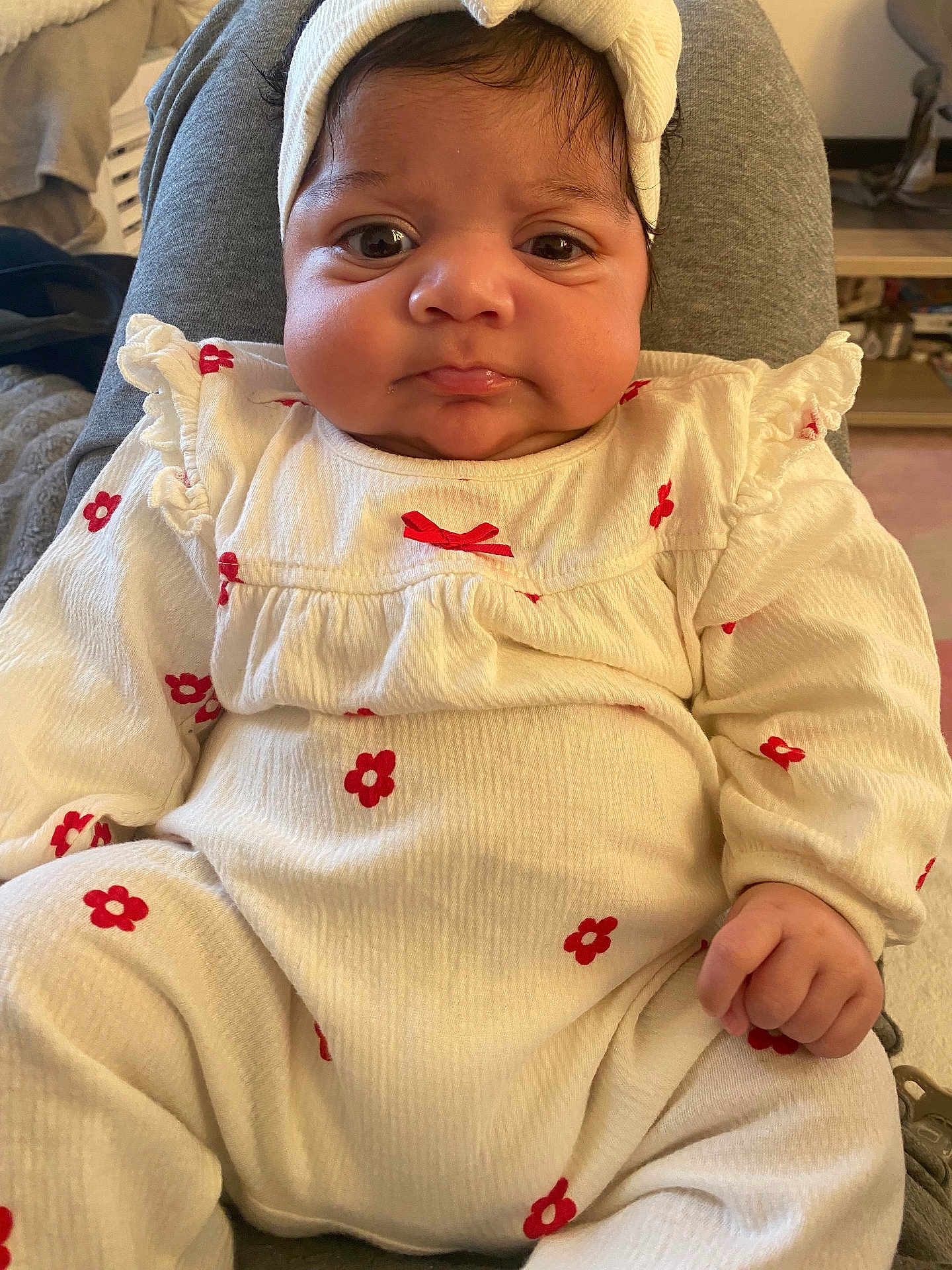 Zoya a rejoint le concours — aidez-le/la à gagner de superbes lots ! baby, infant, child, face, headband, clothing, white_outfit, red_flowers, pout, hand, sitting, indoors, soft_lighting, cute, portrait, young_child, cozy, expression, human, person