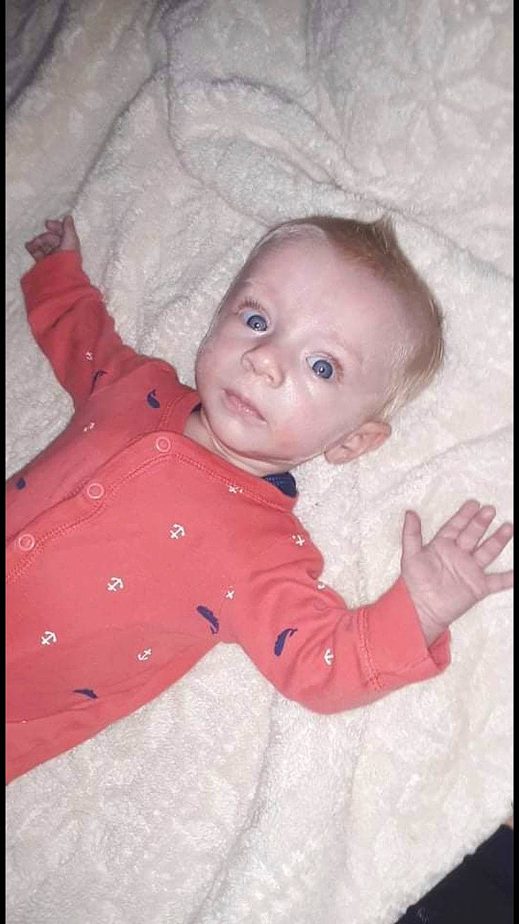 Lewis is registered to the contest to win money with this photo: baby, baby_toddler_clothing, cheek, child, comfort, eye, facial_expression, flooring, happy, iris, linens, lip, nose, pattern, person, pink, room, sitting, skin, sleeve