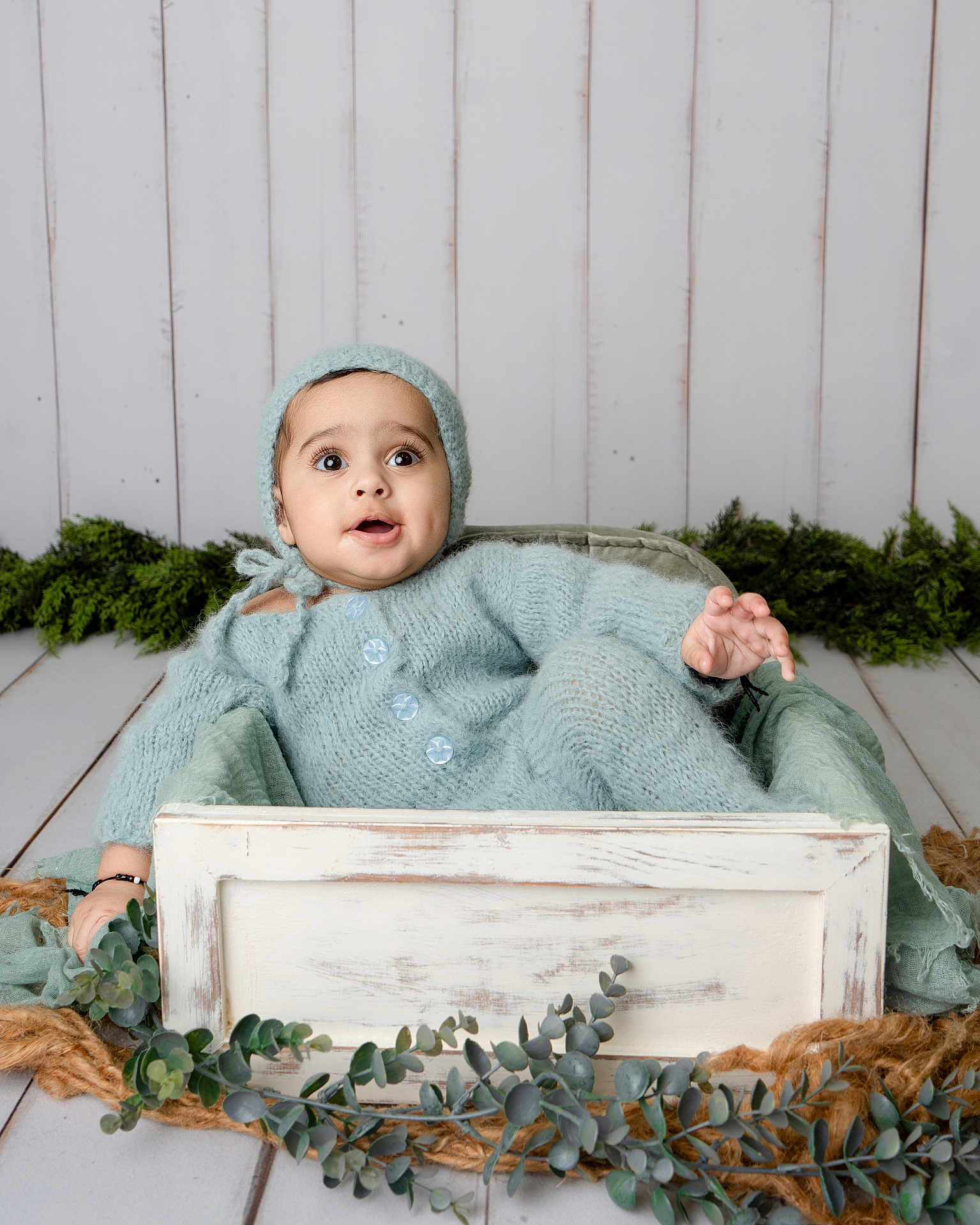 Eesa Abbas joined the competition — help win amazing prizes! baby, blue, buttoned_sweater, child, cozy, crate, cute, expression, floor, greenery, hat, indoors, infant, knitwear, person, plant, portrait, seated, wooden_box, young