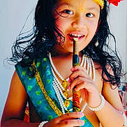 William joined the competition — help win amazing prizes! child, portrait, smiling, traditional_costume, crown, jewelry, flute, musical_instrument, red_flower, long_hair, makeup, cultural_attire, blue_clothing, yellow_skirt, pearl_necklace, bracelets, indoor, seated, colorful, photography