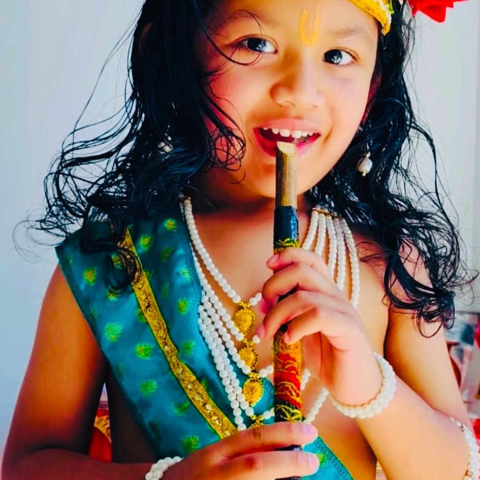 William joined the competition — help win amazing prizes! child, portrait, smiling, traditional_costume, crown, jewelry, flute, musical_instrument, red_flower, long_hair, makeup, cultural_attire, blue_clothing, yellow_skirt, pearl_necklace, bracelets, indoor, seated, colorful, photography