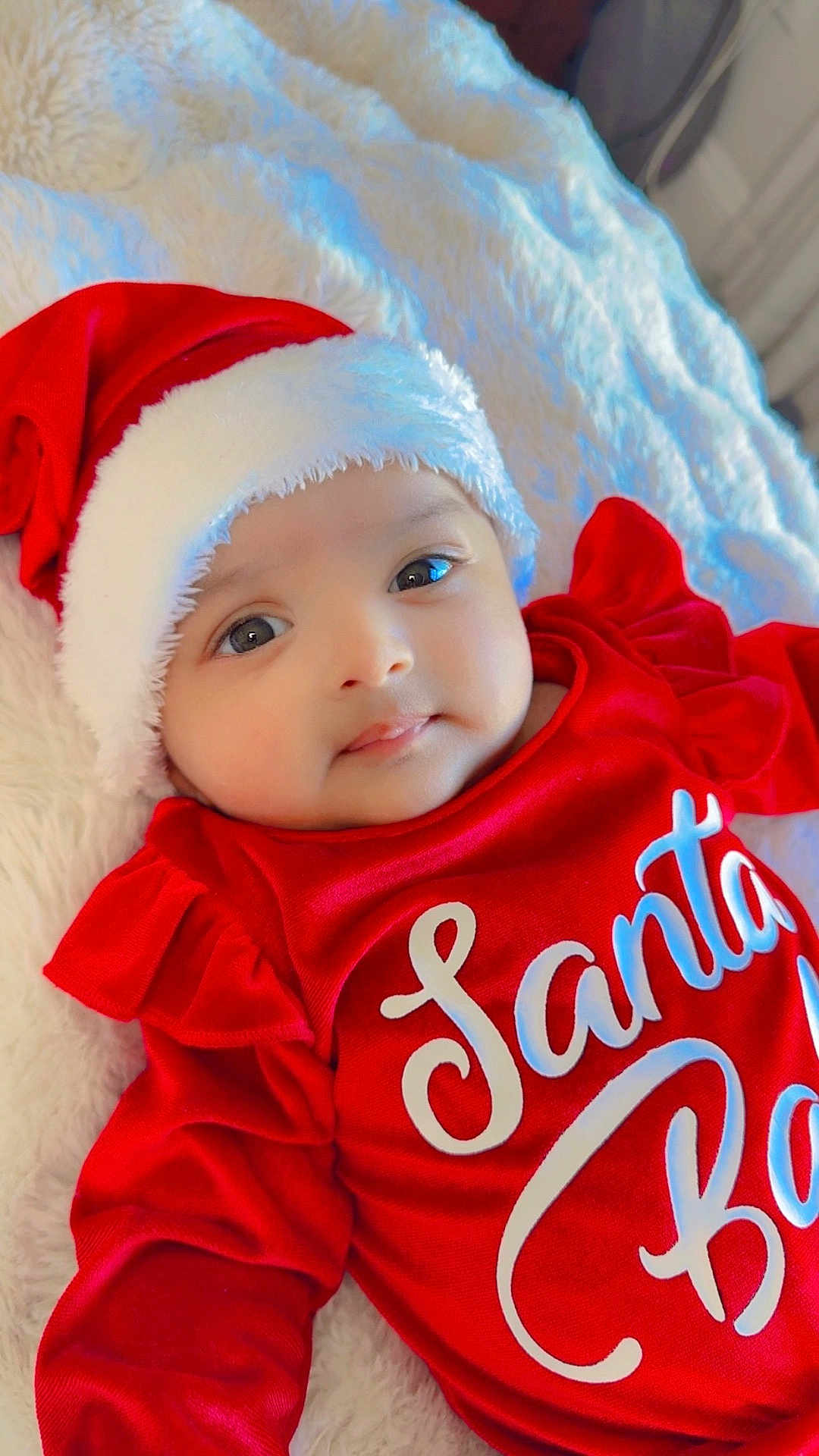 Aveera joined the competition — help win amazing prizes! baby, child, infant, santa_hat, red_clothing, festive, holiday, cute, smile, face, portrait, lying_down, blanket, soft_texture, indoors, warm, comfortable, young_child, christmas, holiday_season