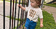 Adhara is registered to the contest to win money with this photo: casual_clothing, child, concrete, curious, daylight, expression, fence, grass, hair_tied, jeans, leopard_print, nature, outdoor, person, residential, shirt, side_view, standing, toddler, young_child