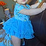 toddler, child, blue_dress, boots, couch, indoor, furniture, curly_hair, earrings, watch, room, pillow, table, flowers, light, person, standing, holding, cute, expression
