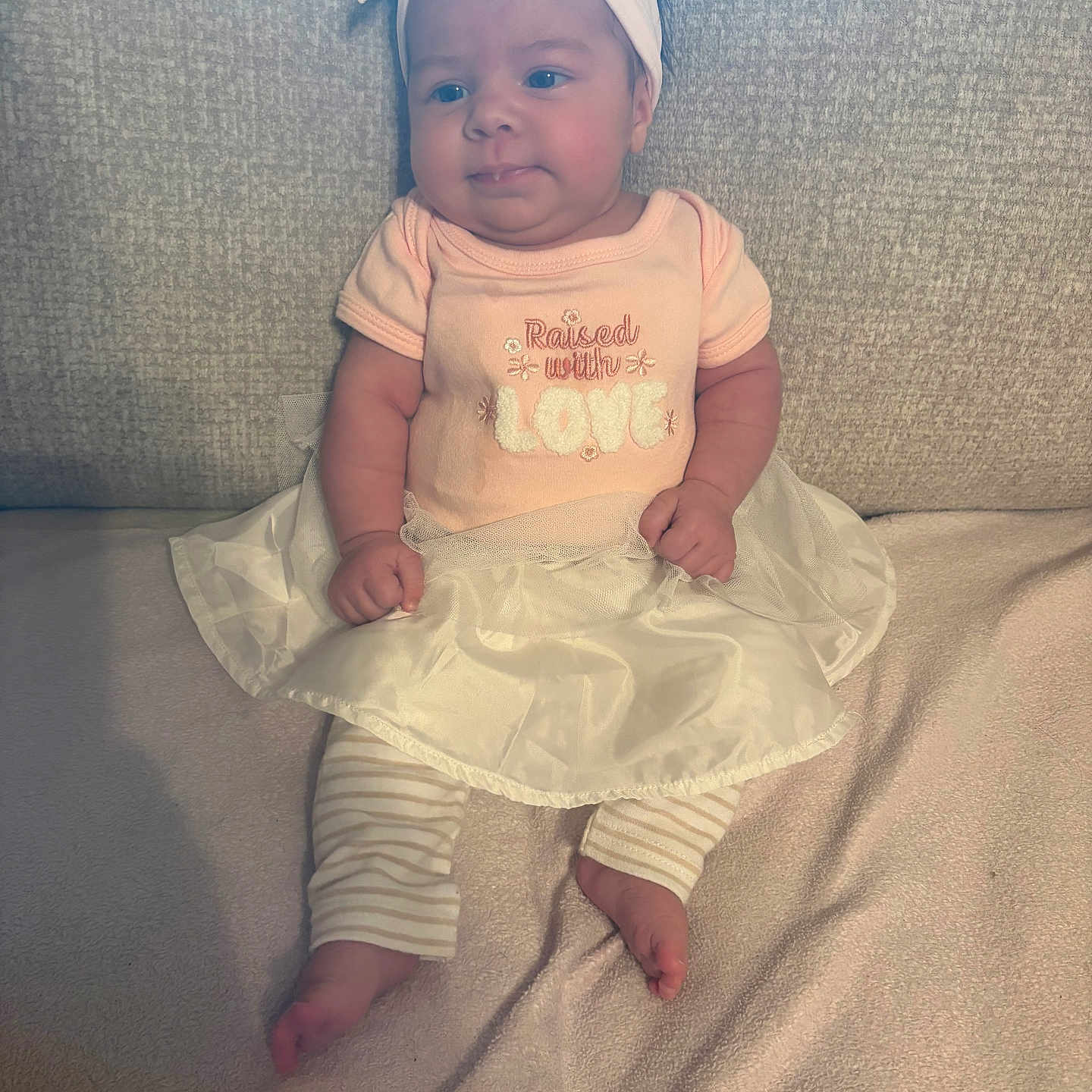 Magnolia is registered to the contest to win money with this photo: baby, infant, child, person, headband, pink_clothing, tutu, striped_pants, barefoot, couch, blanket, soft_texture, sitting, cute, portrait, indoors, happy, smile, chubby_cheeks, comfortable
