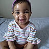 baby, child, smiling, happy, portrait, indoor, bed, sitting, cross_legged, headband, bow, purple, striped_clothing, long_sleeves, infant, face, eyes, teeth, bedroom, photography