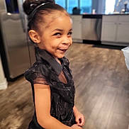 Morgan joined the competition — help win amazing prizes! child, girl, portrait, smiling, side_glance, indoors, kitchen, home, black_dress, hair_bun, headband, standing, facial_expression, playful, fashion, wooden_floor, cabinets, appliance, natural_light, photography