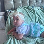 baby, bed, bedroom, blanket, blue, bow, child, clothing, cozy, curious, cute, headband, indoors, infant, lying_down, person, portrait, soft_texture, tufted_headboard, white