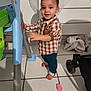 toddler, child, barefoot, plaid_shirt, blue_pants, indoor, tile_floor, plastic_chair, standing, curious, smiling, young_child, person, home, toy, footwear_absent, furniture, baby, casual_clothing, expression