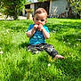 Naël a rejoint le concours — aidez-le/la à gagner de superbes lots ! toddler, child, grass, flowers, blue_shirt, black_pants, barefoot, outdoor, garden, sunny, greenery, building, sitting, playful, cute, nature, daylight, person, face, young_child