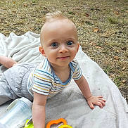 Marceau participe au concours pour gagner de l'argent avec cette photo : baby, child, toy, blanket, outdoor, grass, water_bottle, smile, blue_eyes, striped_shirt, shorts, hand, face, person, daylight, playing, cute, young, nature, happy