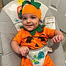Amarii is registered to the contest to win money with this photo: baby, child, pumpkin_costume, orange_clothing, green_hat, smiling, sitting, bouncer, infant, portrait, indoors, playful, happy, face, hands, baby_gear, cushion, colorful, costume, photography
