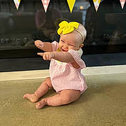 Gwendolyn is registered to the contest to win money with this photo: baby, child, infant, yellow_bow, pink_outfit, pointing, smiling, sitting, floor, decorative_flags, indoor, happy, cute, playful, headband, cheerful, portrait, young_child, celebration, fun