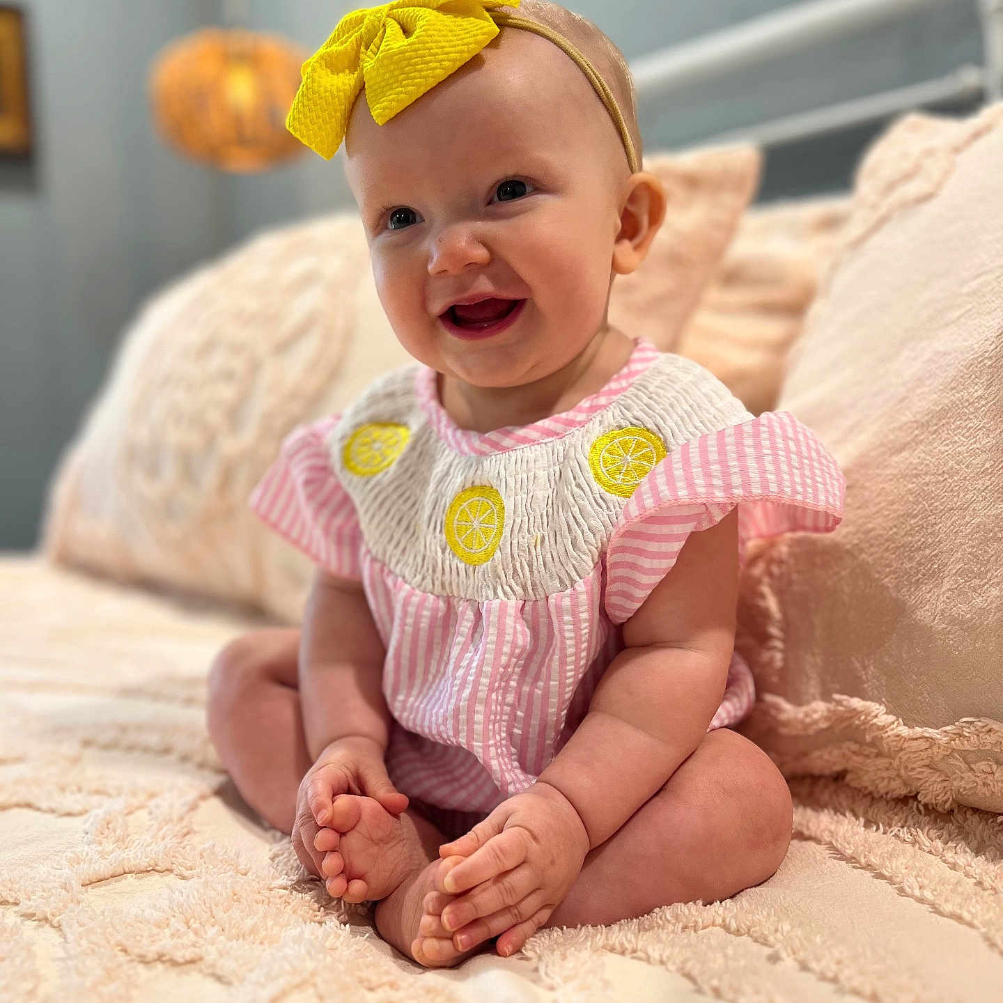 Gwendolyn is registered to the contest to win money with this photo: baby, bedspread, child, cozy, cross_legged, cute, decor, furniture, happy, headband, indoors, infant, person, pink_clothing, portrait, sitting, smile, soft_lighting, texture, yellow_bow