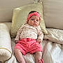 baby, infant, bed, pillow, pink_clothing, headband, soft_fabric, texture, indoor, person, child, cute, relaxed, portrait, seated, comfortable, floral_pattern, home, cozy, pink_shorts