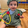 baby, child, infant, doctor_costume, nurse_costume, stethoscope, scrubs, shower_cap, smiling, happy, portrait, sitting, floor, indoor, classroom, wood_floor, toy, medical_play, shelving, nursery