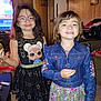 child, children, girl, smile, glasses, dress, denim_jacket, indoor, room, television, toy, baby, car_seat, wood_paneling, furniture, happy, portrait, standing, person, family