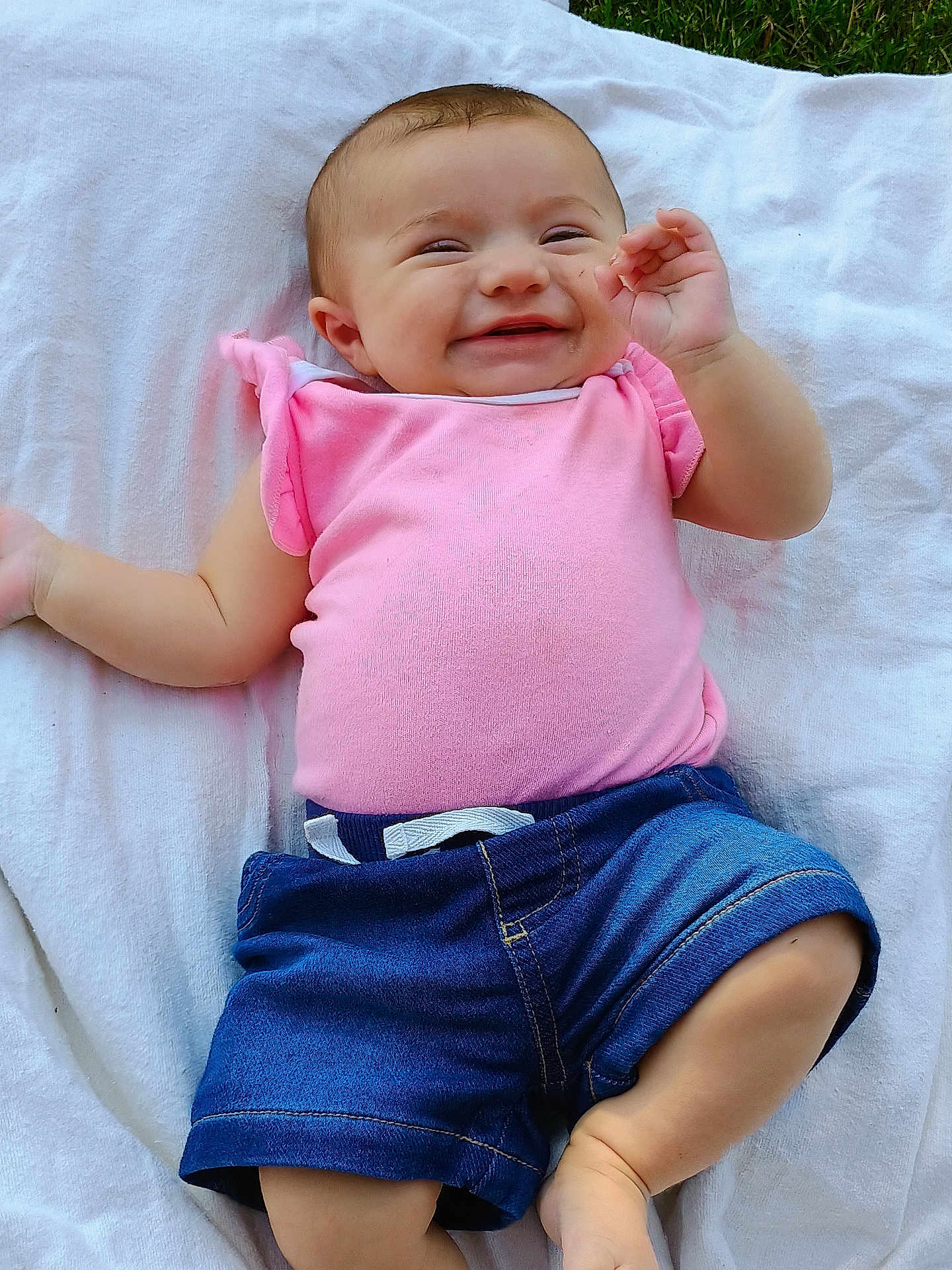 Estella joined the competition — help win amazing prizes! baby, child, smiling, pink_shirt, denim_shorts, blanket, outdoor, grass, happy, cute, infant, portrait, lying_down, casual_clothing, skin, face, hand, foot, toddler, nature