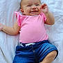 Estella is registered to the contest to win money with this photo: baby, infant, smiling, pink_shirt, denim_shorts, blanket, outdoor, grass, happy, cute, child, person, skin, face, hand, foot, casual_clothing, lying_down, summer, playful