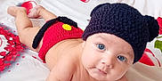 Rayan participe au concours pour gagner de l'argent avec cette photo : baby, black, blanket, blue_eyes, child, curious, cute, expression, funny_hat, heart_pattern, indoors, infant, knitted_hat, knitted_shorts, lying_down, portrait, red, skin, soft_light, young