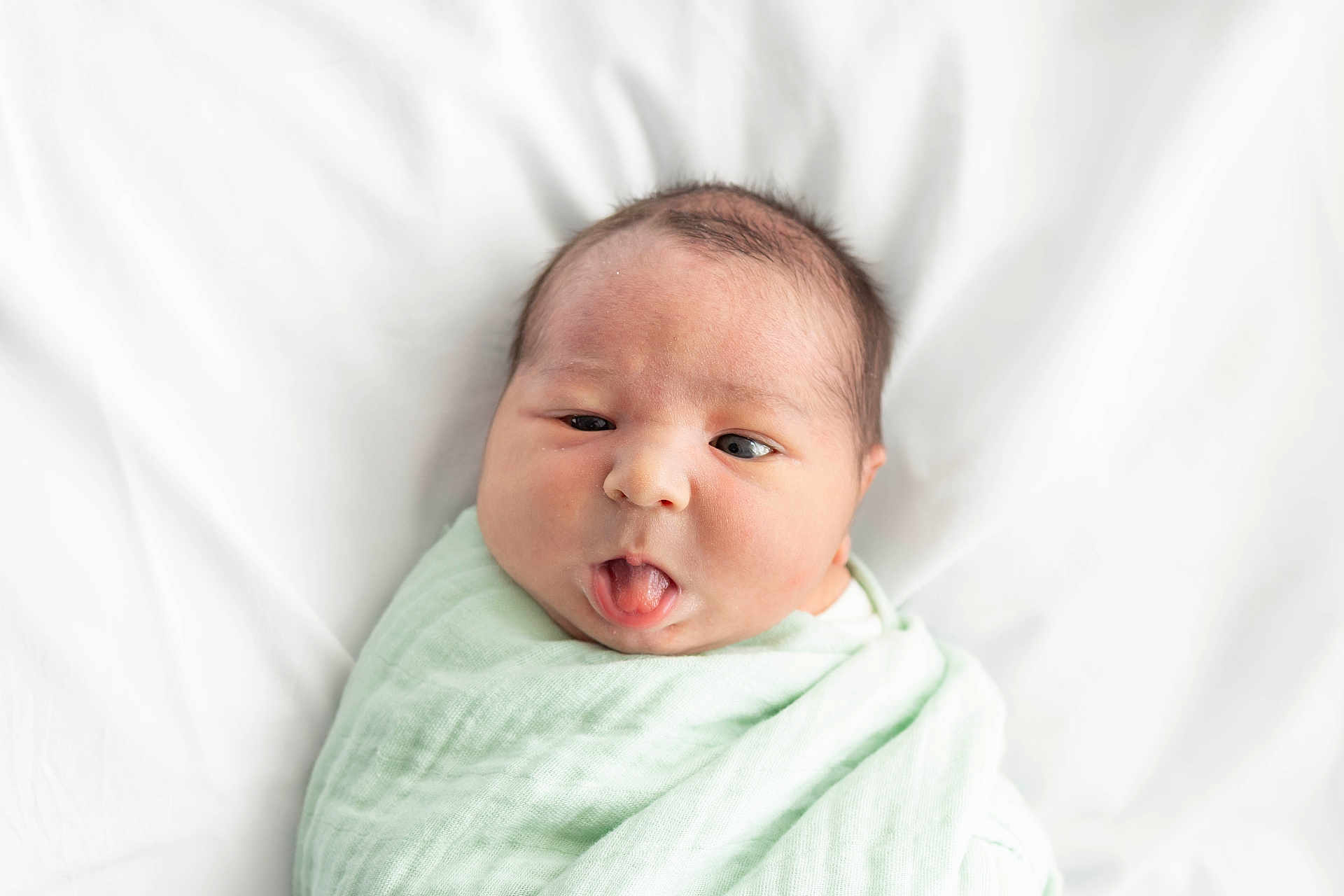 Landon joined the competition — help win amazing prizes! newborn, baby, infant, face, tongue, expression, wrapped, blanket, soft, mint_green, bed, white_background, cute, child, portrait, sleeping_area, skin, head, hair, person