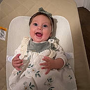 Alice joined the competition — help win amazing prizes! baby, infant, smiling, headband, dress, floral_pattern, tights, bouncer, seat, face, hands, wide_eyes, indoor, door, wood_floor, happy, portrait, fabric, cute, head