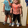toddler, child, standing, door, blue_shirt, butterfly_shirt, shorts, pants, sneakers, socks, indoor, wood_floor, curly_hair, smile, funny_text, cute, people, clothing, wall, young