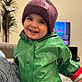 Nader joined the competition — help win amazing prizes! child, toddler, smiling, green_raincoat, purple_beanie, indoor, living_room, television, happy, person, coat, clothing, headwear, cute, portrait, warm_clothing, joyful, face, kid, casual