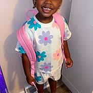 Aniyah joined the competition — help win amazing prizes! child, toddler, smiling, portrait, standing, indoor, backpack, pink_backpack, flower_pattern, colorful_clothing, braided_hair, hair_buns, earrings, shoes, clogs, hallway, door, light_switch, wood_floor, school_ready